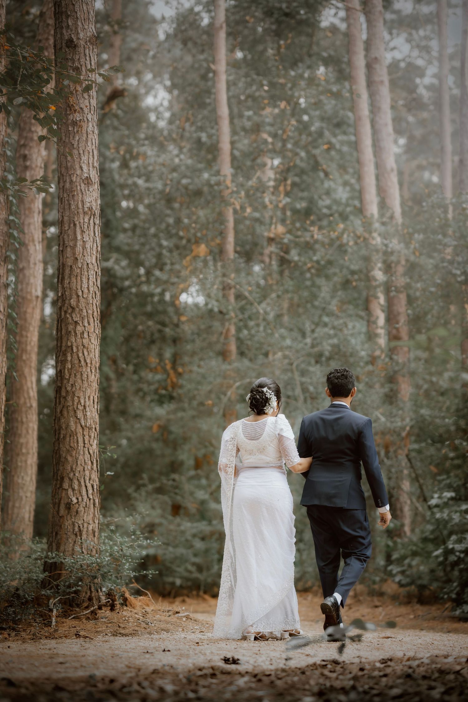 A newlywed couple walking away from camera through a peaceful wooded path.