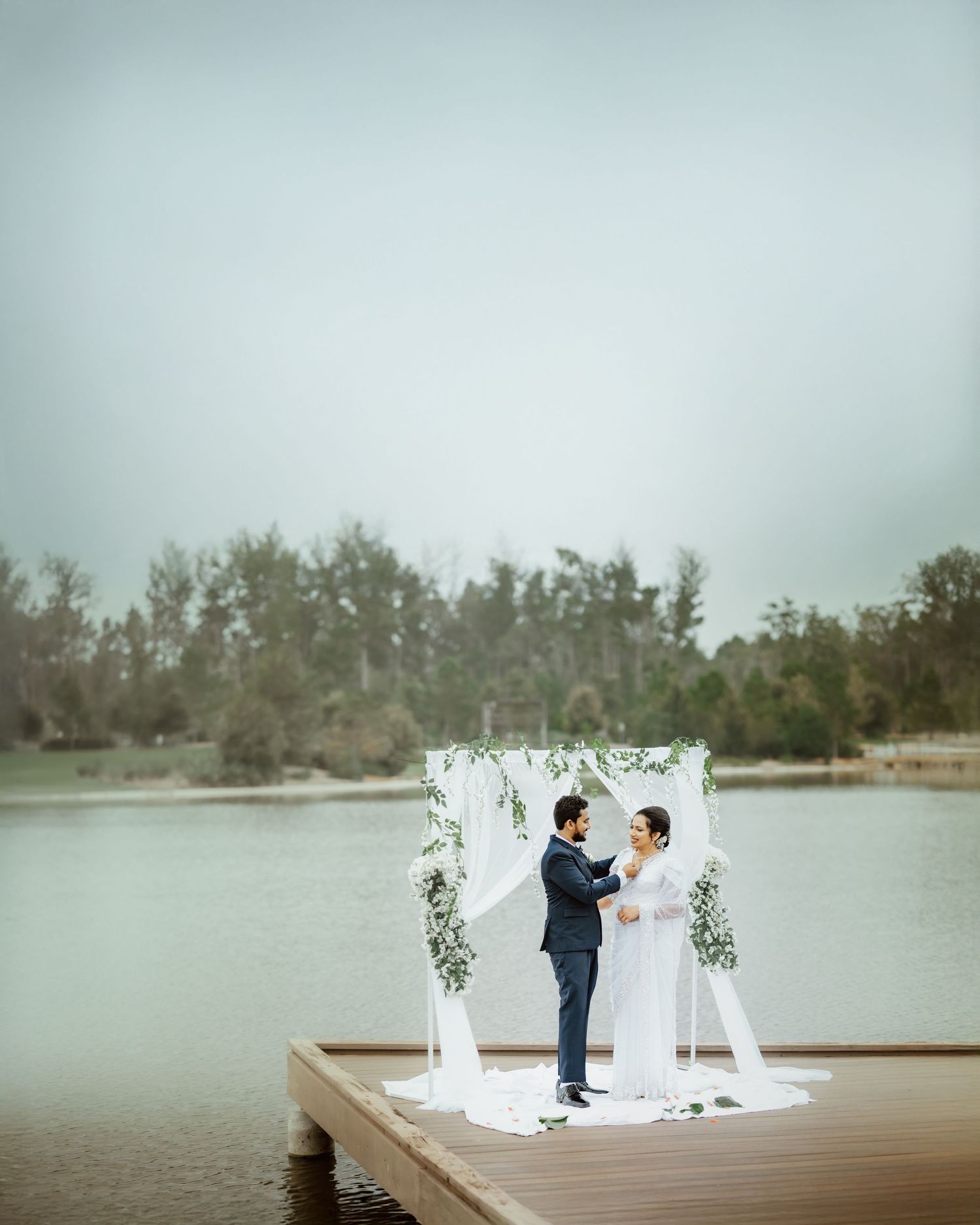 A lakeside wedding ceremony setup with white arch and floral decorations on a misty day.