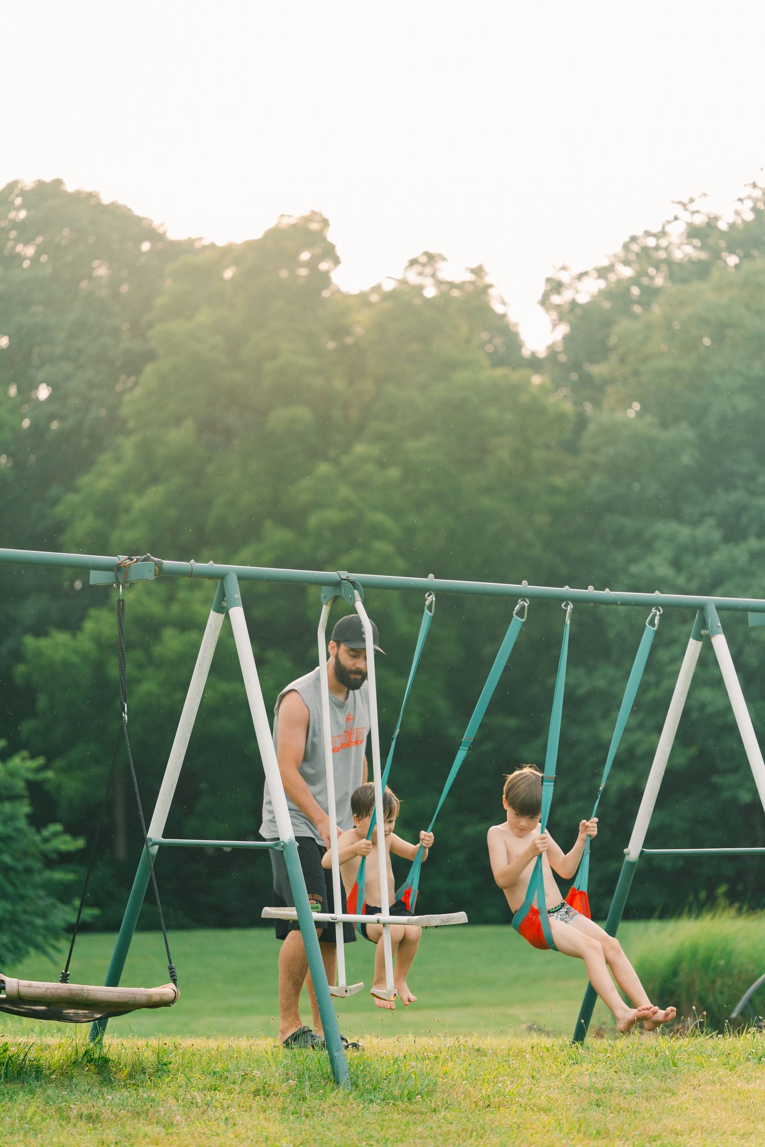 Family plays together on a swing set during golden hour in a backyard.