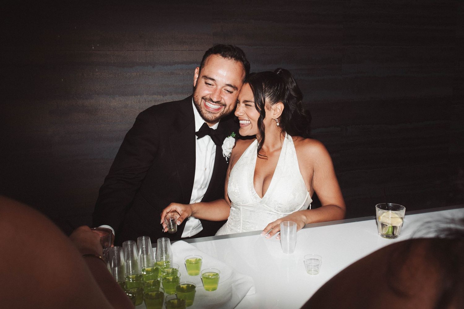 Couple in formal attire sharing intimate moments at a dimly lit dining table with glowing green drinks.