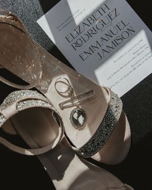 Wedding accessories including sparkly shoes and a novel by Elizabeth Rodriguez lie artfully arranged on a dark surface.