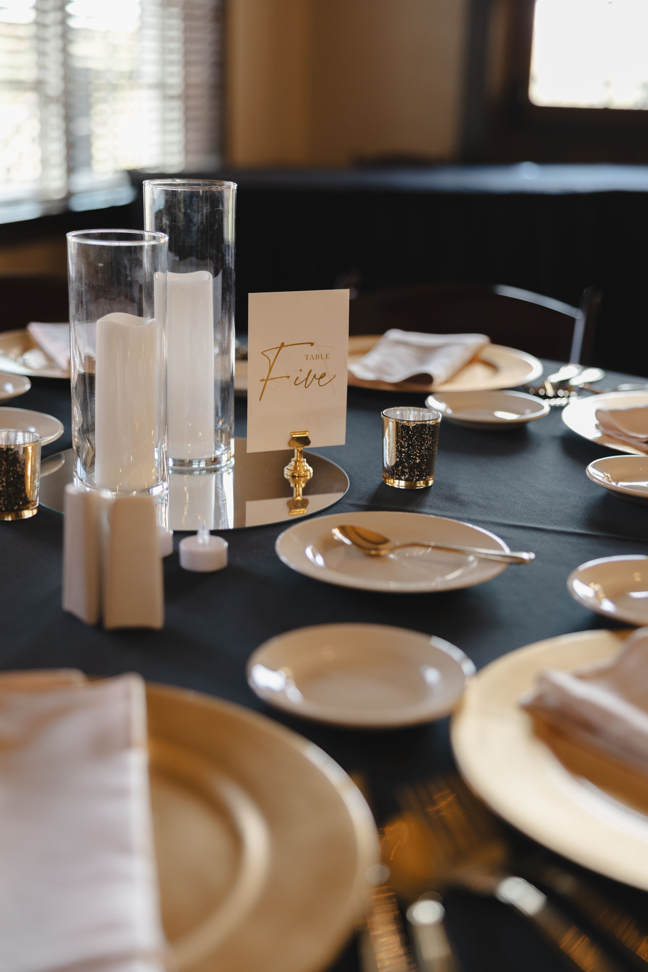 Elegant table setting with white plates, tall glasses and gold accents on a dark tablecloth.