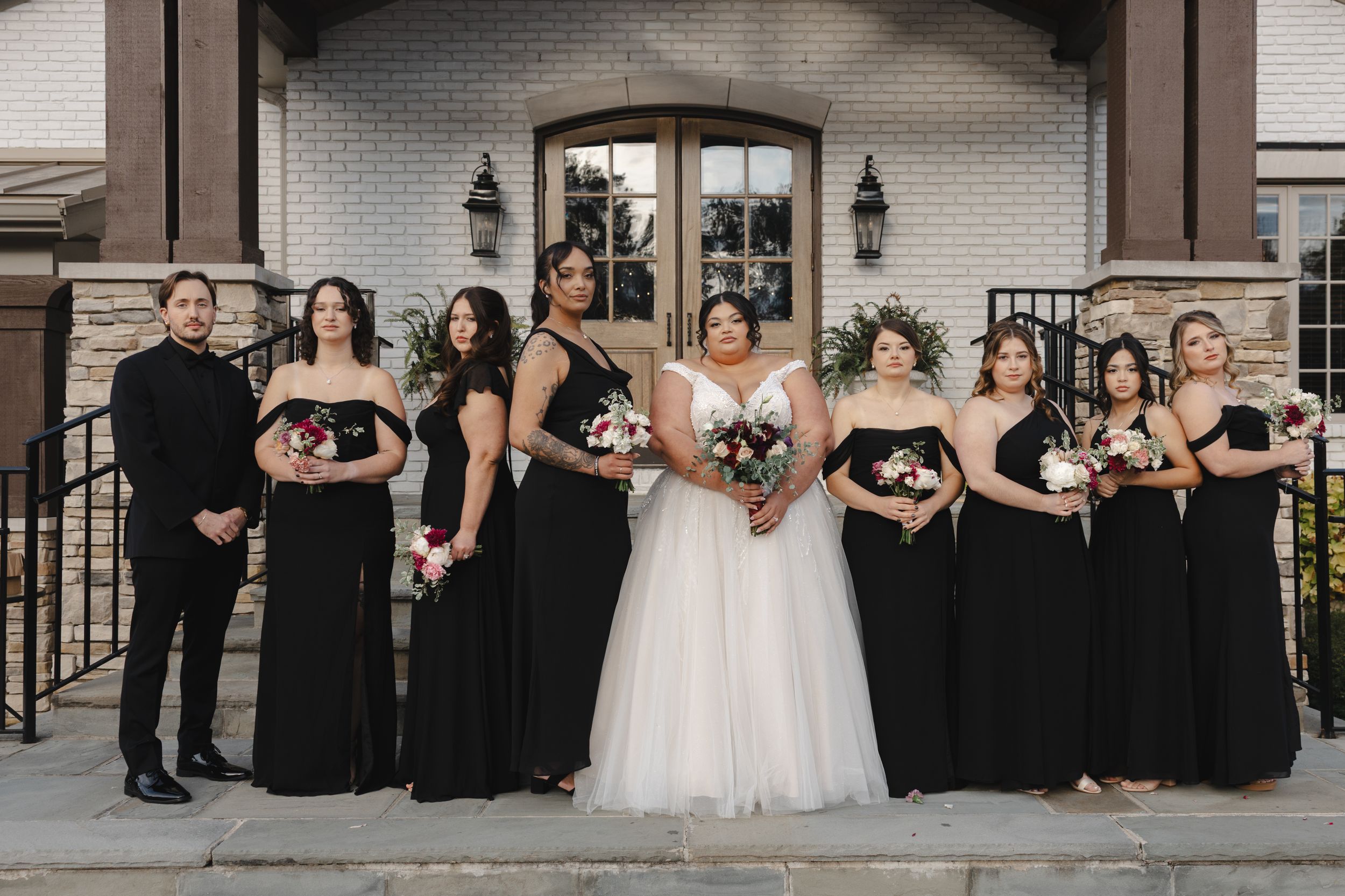 Wedding party in formal attire standing in front of a brick building entrance.