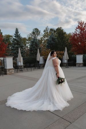 A flowing white wedding dress train creates a dramatic sweep across an outdoor patio with autumn trees in the background.