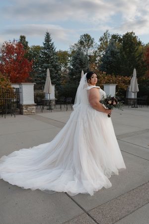 A flowing white wedding dress with a long train photographed outdoors on a concrete patio with autumn trees in background.