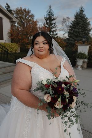 A bride in a white off-shoulder gown holds a vibrant burgundy and blush bouquet with cascading greenery on her wedding day.