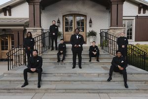 Wedding party members in dark formal attire posed casually on outdoor stone steps.