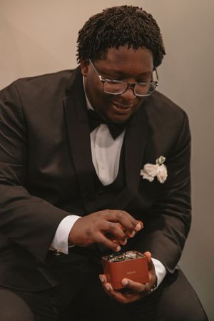 A person in a black suit jacket smiles while looking down at something in their hands during a wedding.