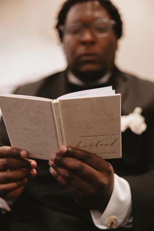 Close-up shot of hands holding a small book or wedding vows in warm lighting.