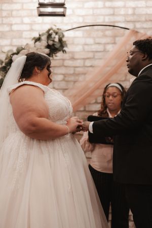 A wedding ceremony shows a couple exchanging rings while an officiant presides over the intimate moment.