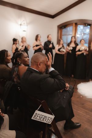 Wedding guests in formal attire seated in rows with a 'Reserved' sign visible during an indoor ceremony.