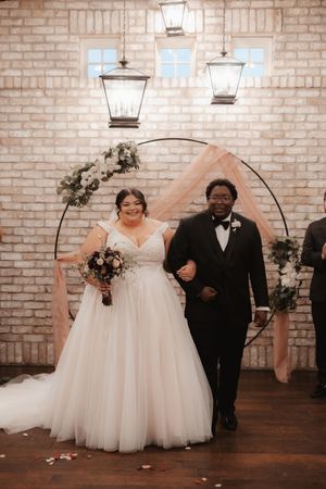 A romantic wedding couple walks together in a rustic brick-walled venue illuminated by elegant lantern lighting.