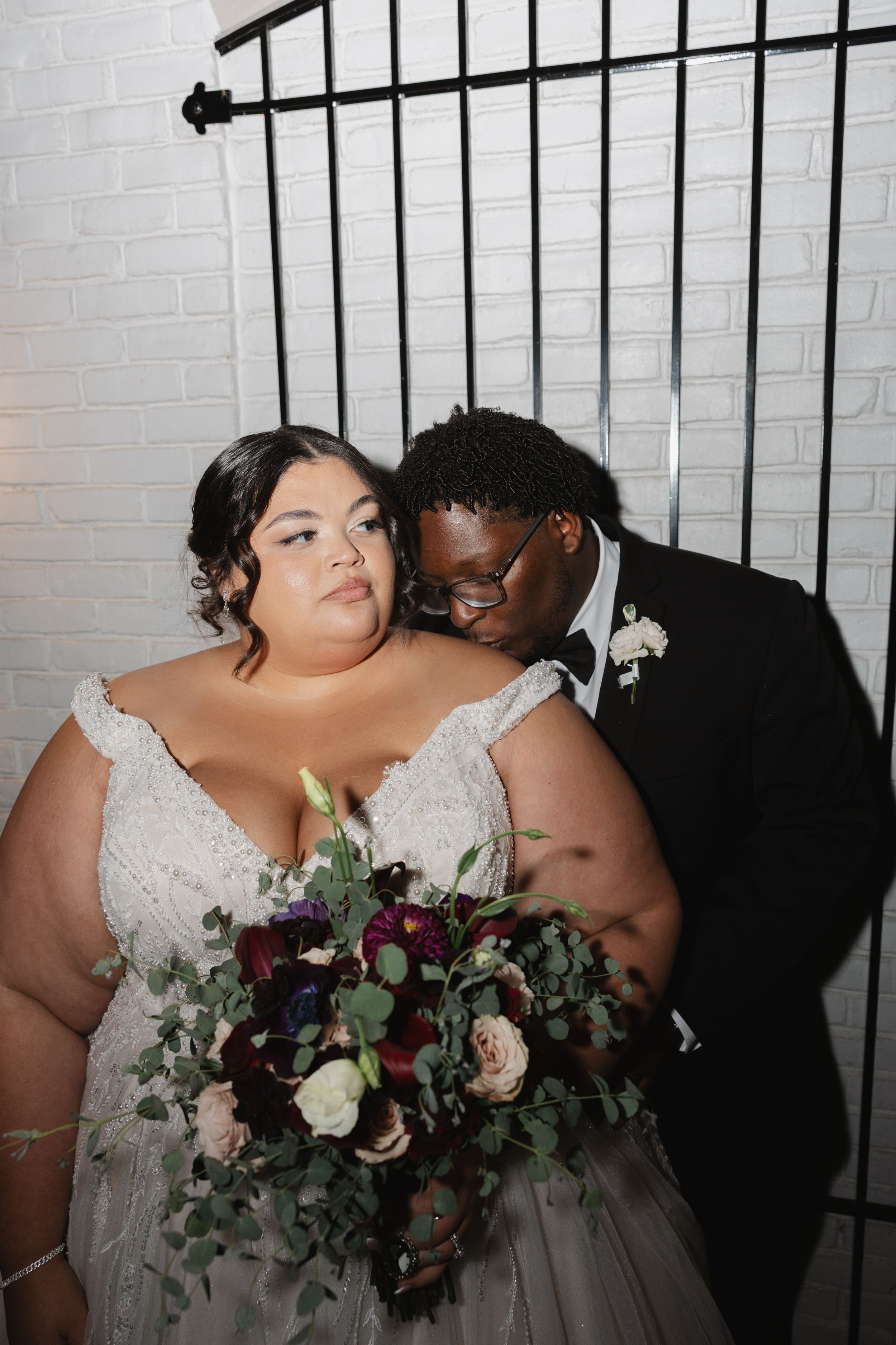A romantic wedding portrait against a white brick wall with a beautiful floral bouquet.