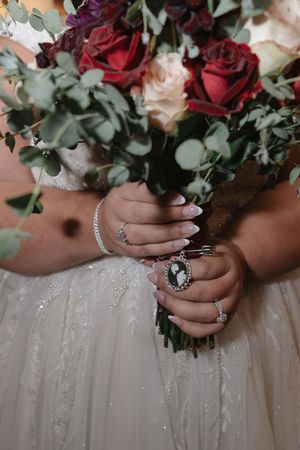 A detailed shot of hands holding a burgundy and blush rose wedding bouquet against a sparkly dress.