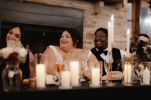 A warmly lit wedding reception venue with glowing candles and guests seated at long tables in an intimate setting.