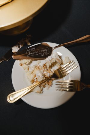 Empty plates with cake crumbs and gold forks on a dark surface after a wedding reception.