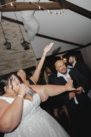 Wedding celebration with guests dancing and raising their arms in joy under string lights at an indoor venue.