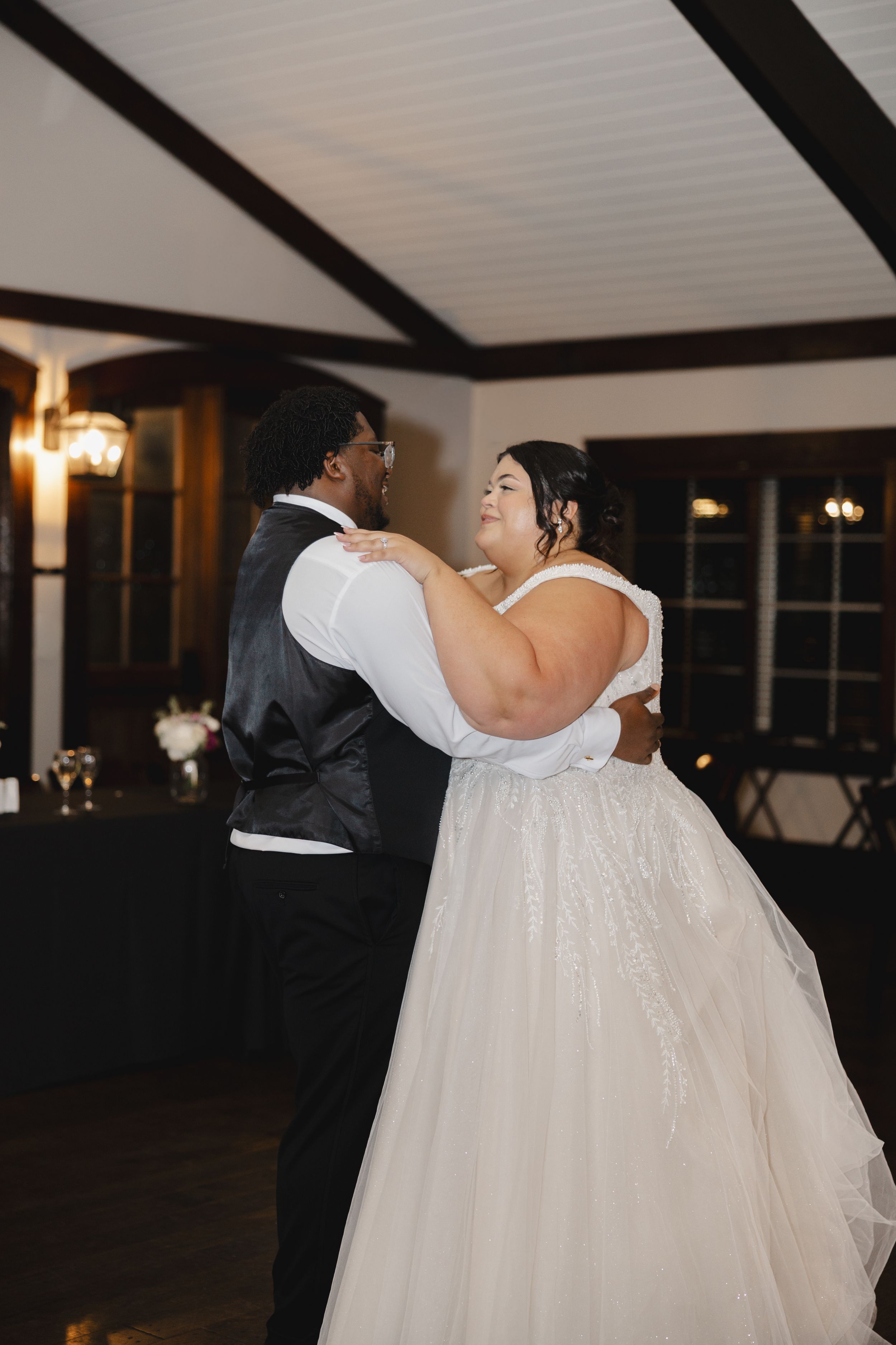 A couple dancing together at their wedding reception in a venue with exposed wooden beams and warm lighting.