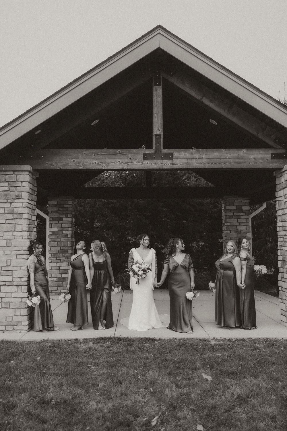 Black and white photo of wedding party members lined up under rustic stone pavilion in casual outdoor setting.