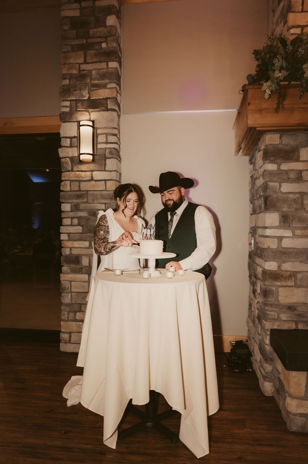 A couple sits at a white-clothed table in a rustic setting with stone columns and warm lighting.