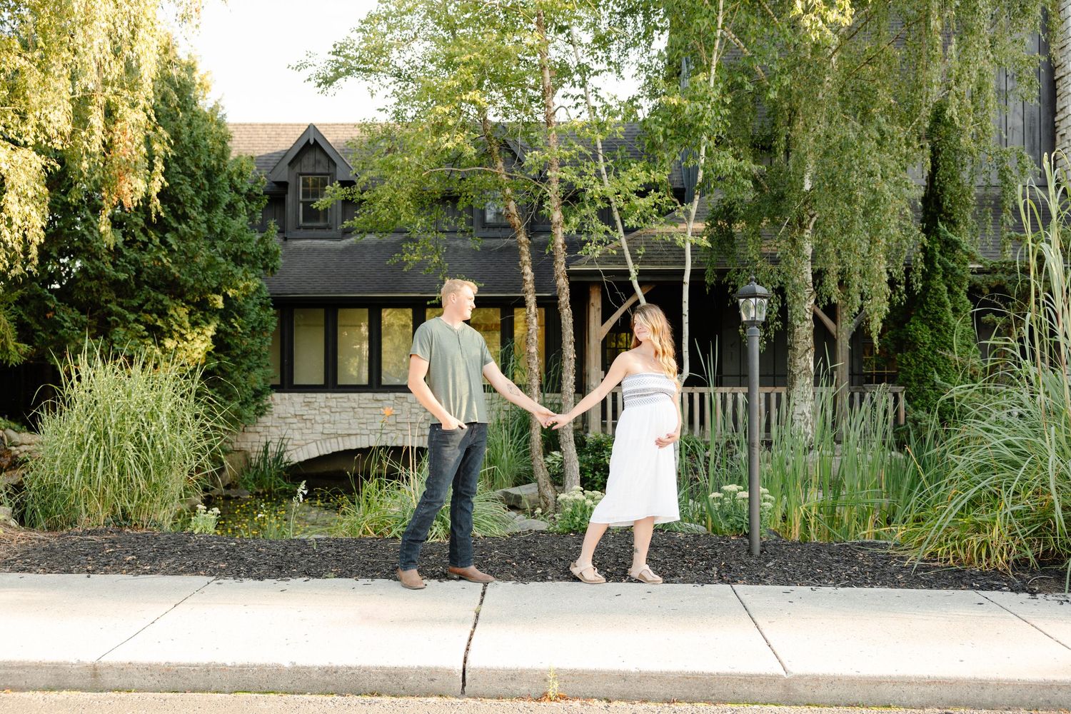 A couple walks together through a scenic garden path with lush greenery and trees on a sunny day.
