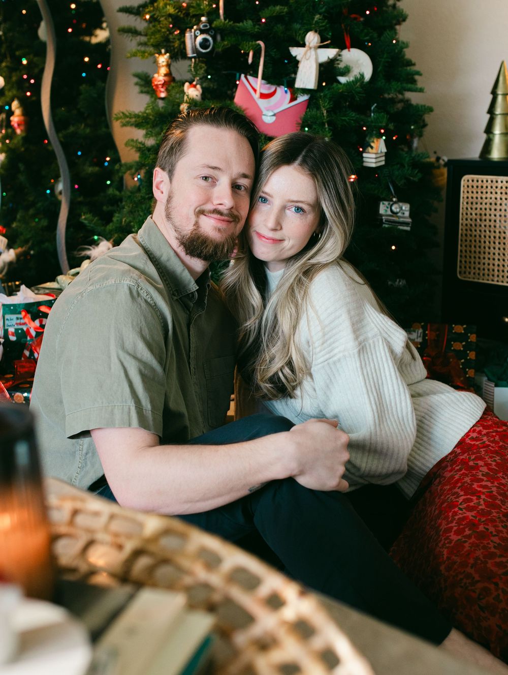 Couple sharing intimate moments in front of decorated Christmas tree with twinkling lights and ornaments.