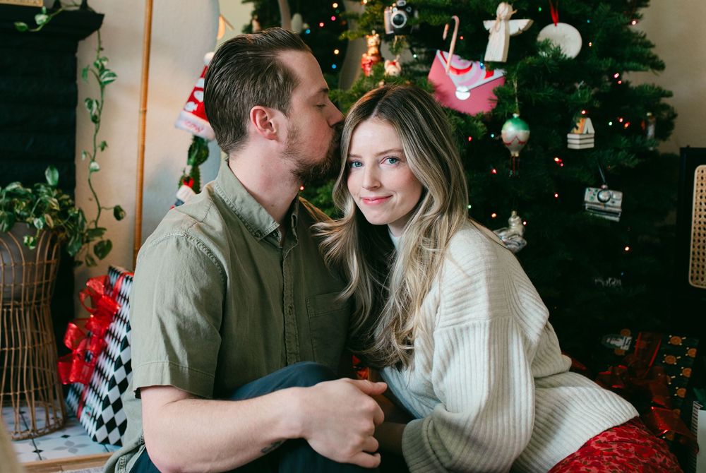 A couple shares romantic moments in front of a decorated Christmas tree during a holiday photoshoot.