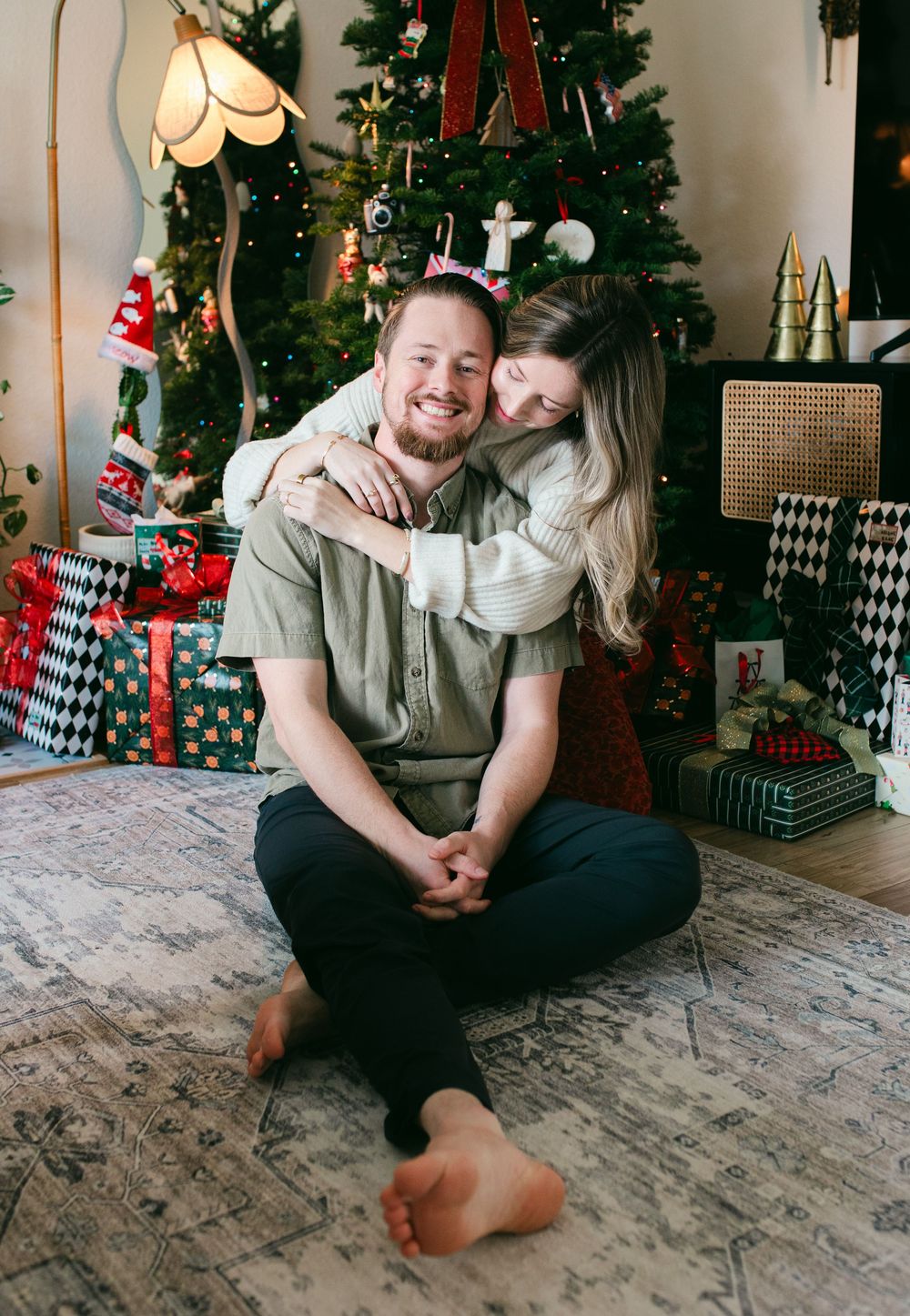 Couple sharing intimate moments in front of a decorated Christmas tree in a cozy living room setting.