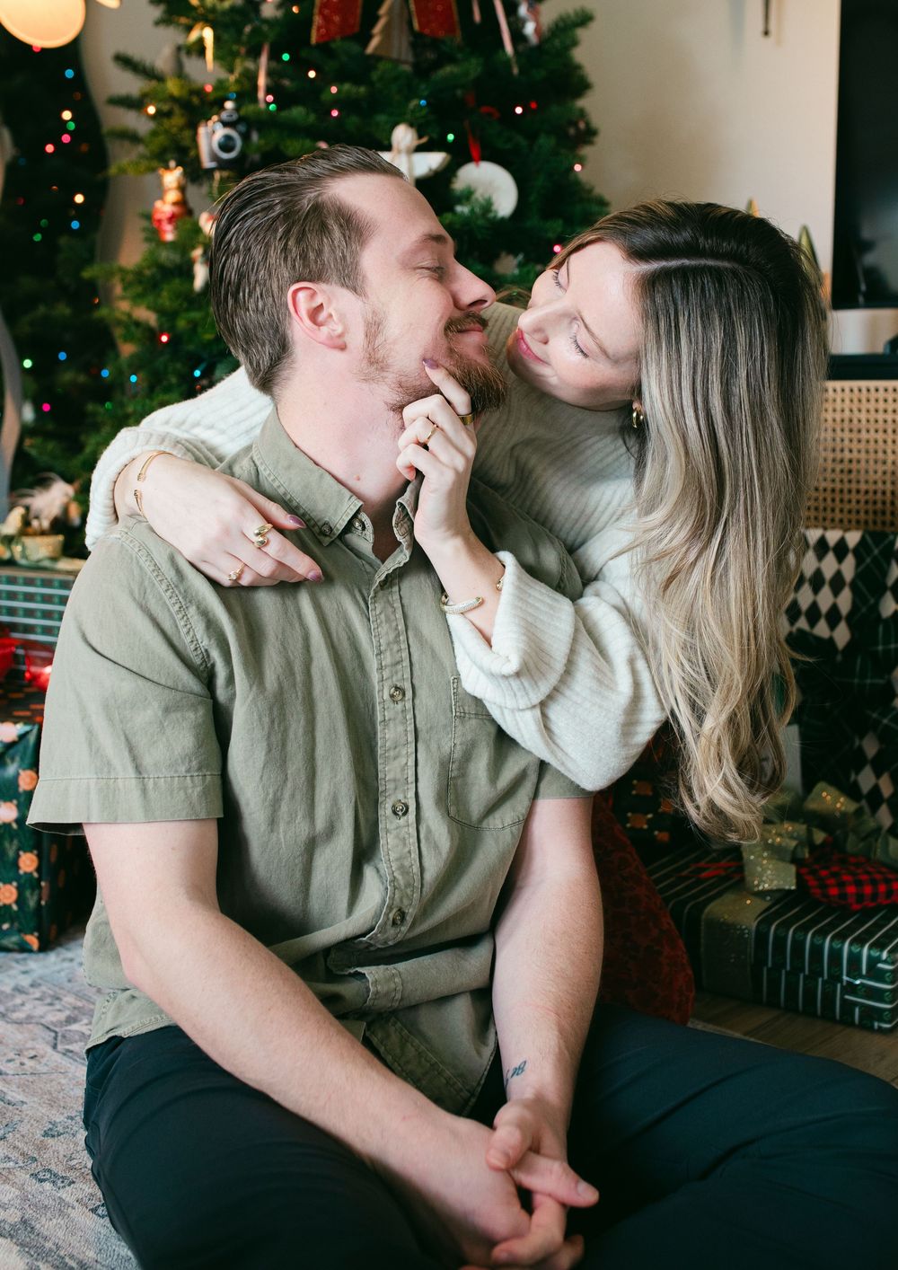 Romantic couple embracing and laughing together near a Christmas tree with wrapped presents.