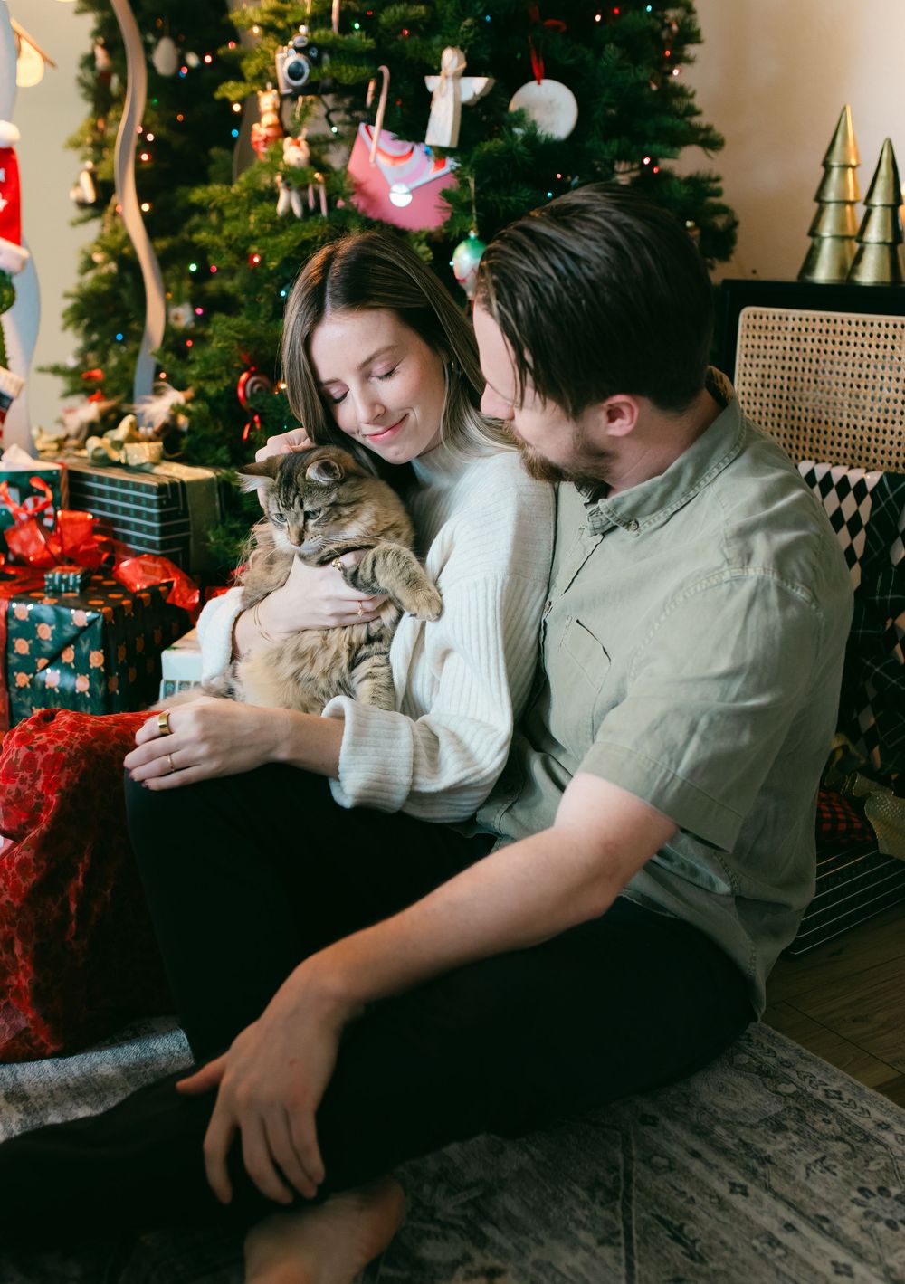 Couple embraces on couch with Christmas tree and holiday decorations in background.