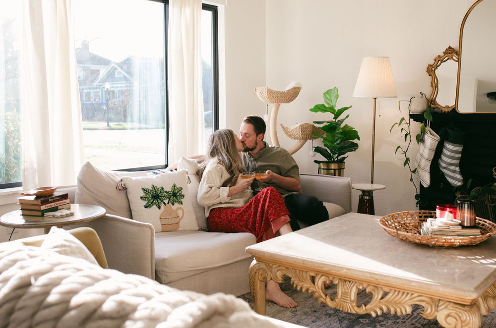 A cozy living room interior with white walls, potted plants, and natural light streaming through windows.