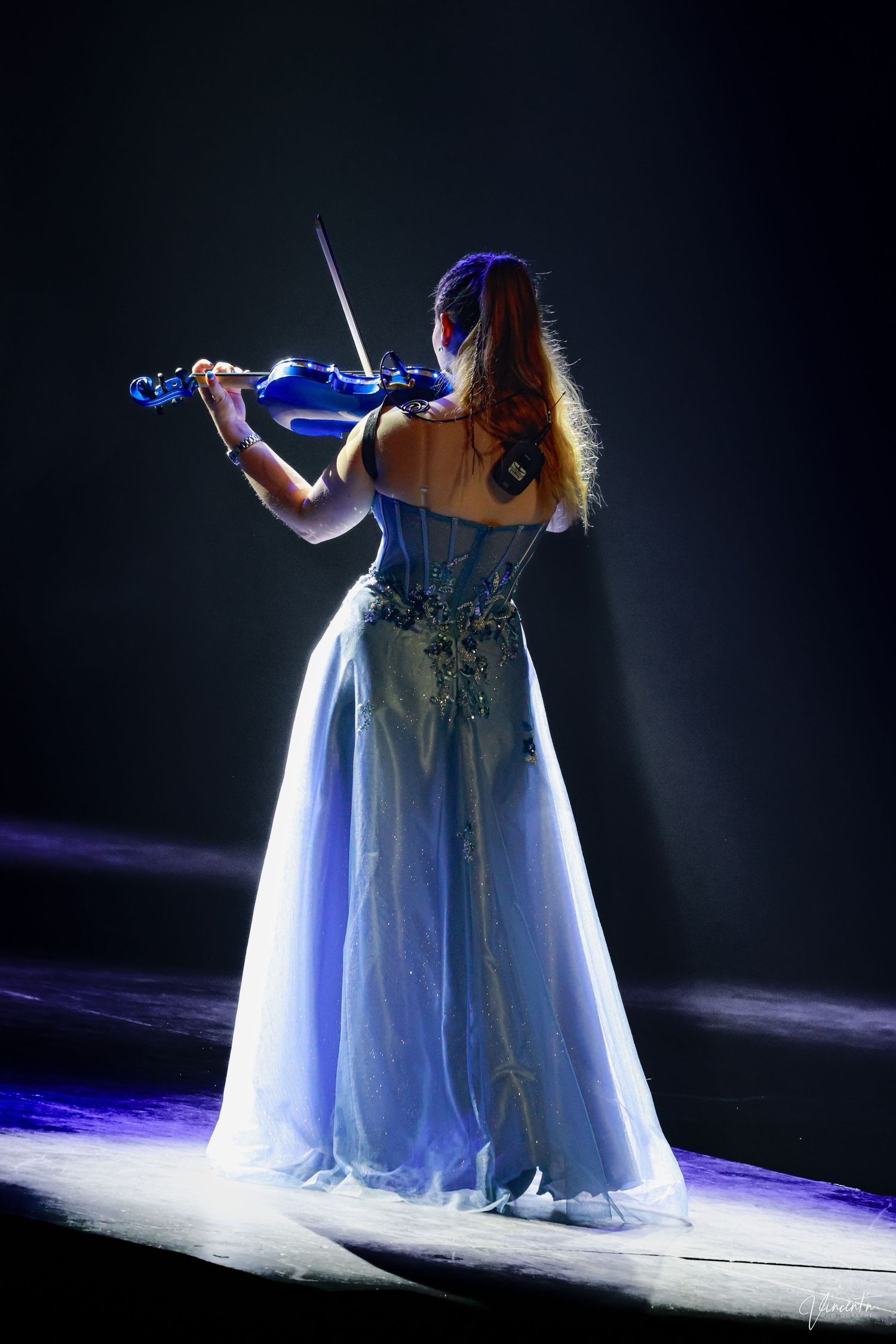 Performer in flowing white gown dances under dramatic blue stage lighting.