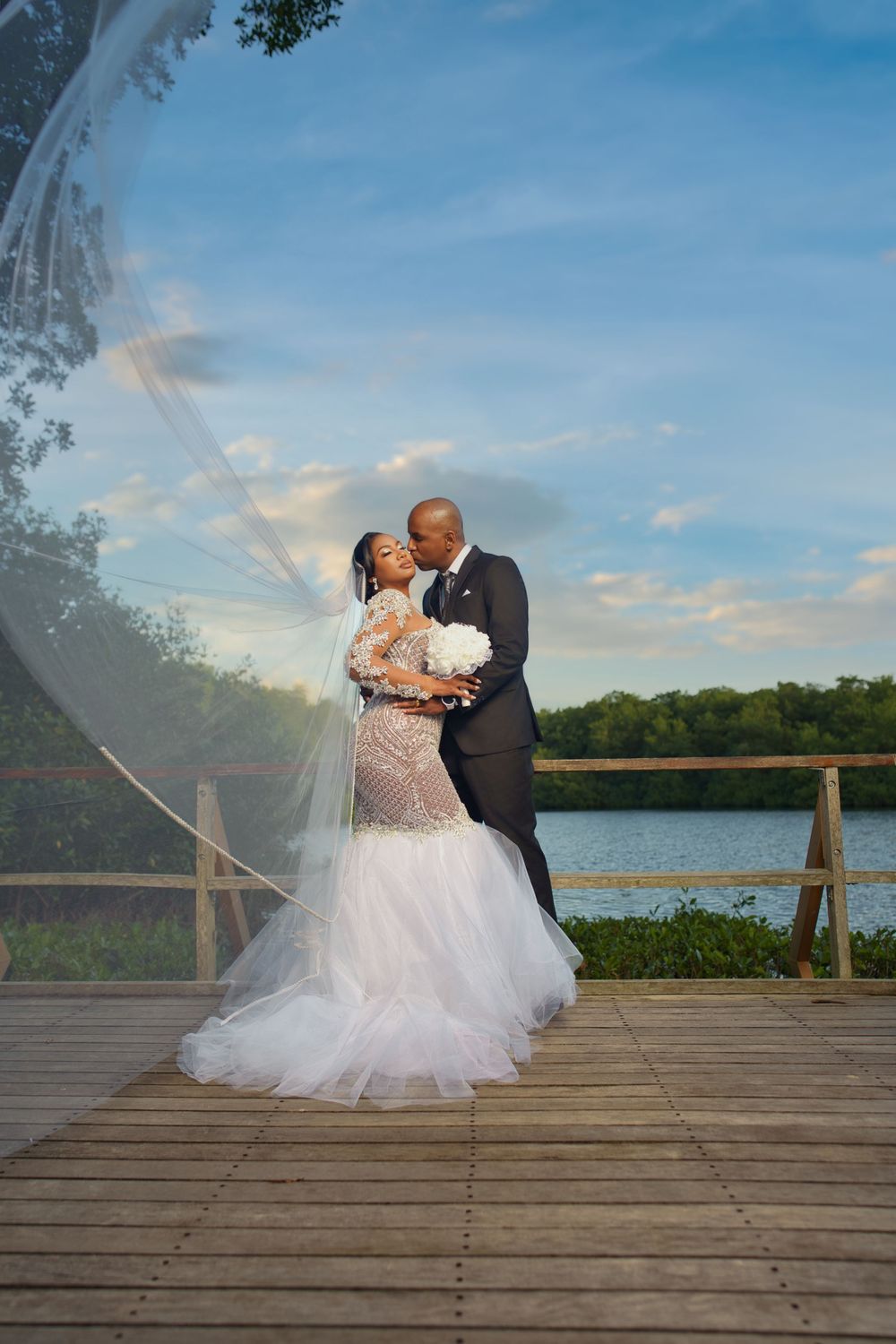 A romantic wedding couple shares intimate moments on a wooden deck overlooking a scenic lake during their photoshoot.