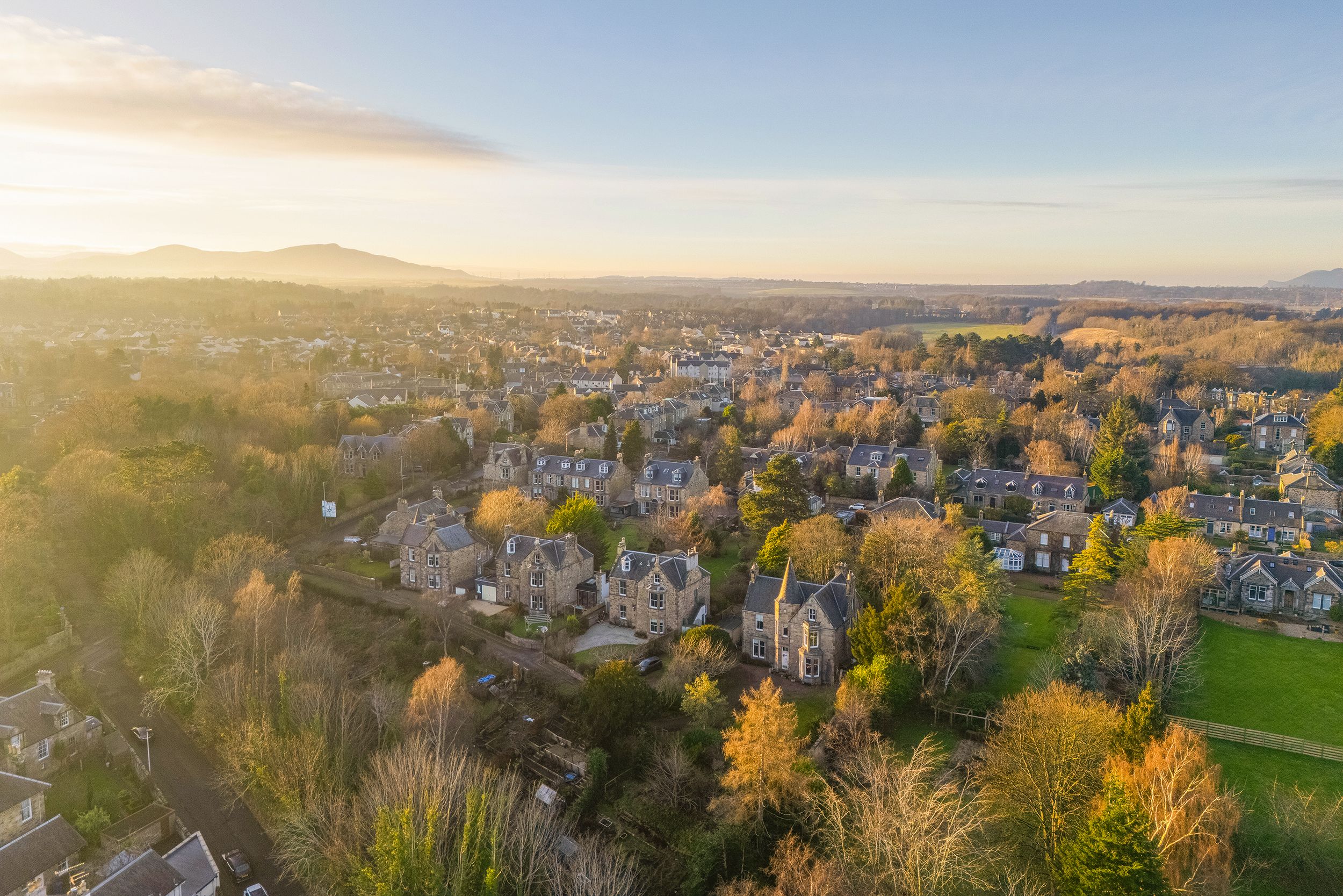 Aerial panoramic view of a suburban neighborhood with autumn foliage and rolling hills during golden hour sunset.