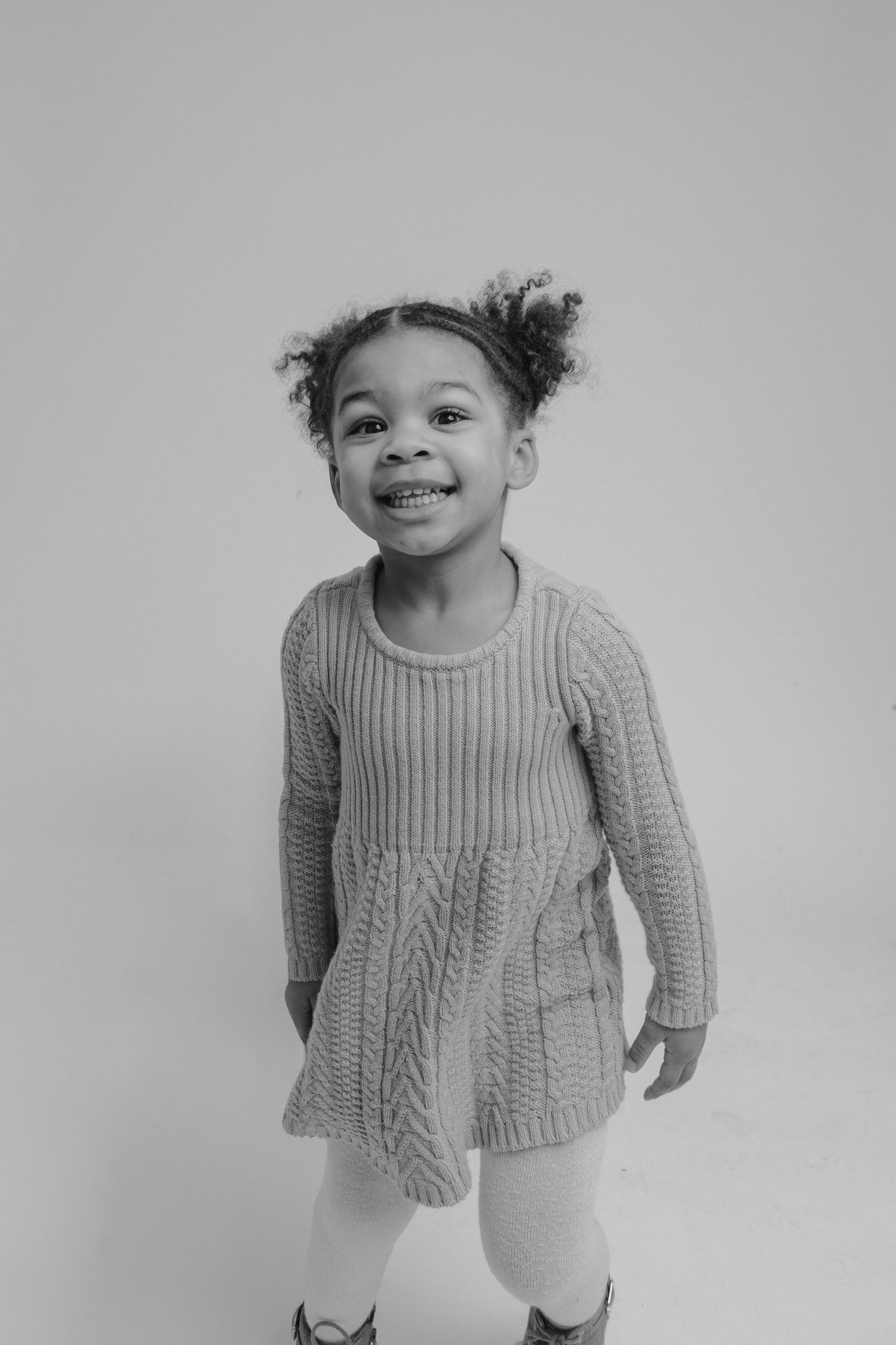 Black and white photo series showing a small child in a cozy knit sweater making playful expressions.