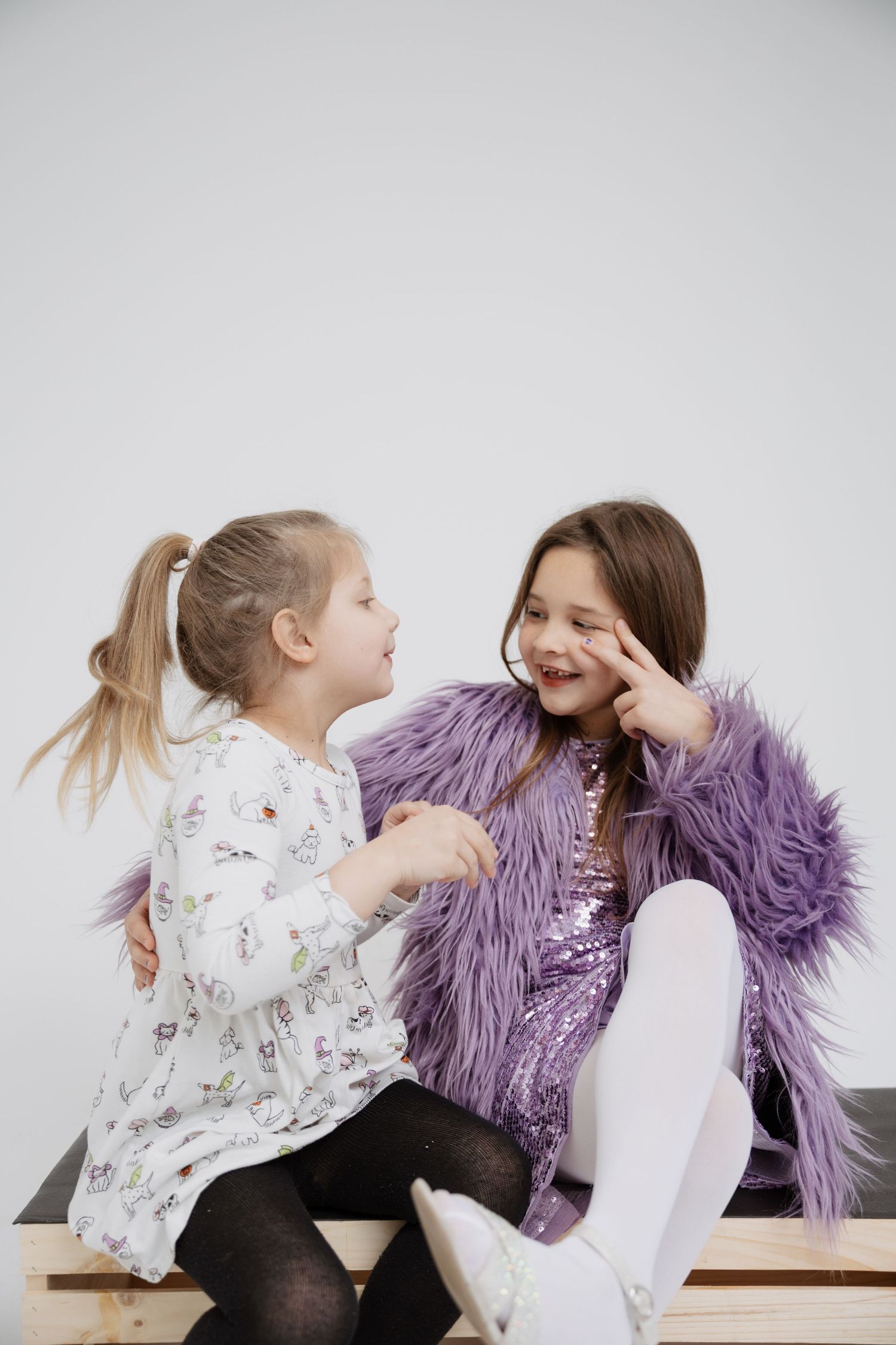 Two children in casual attire share a playful moment while sitting together on a bench.