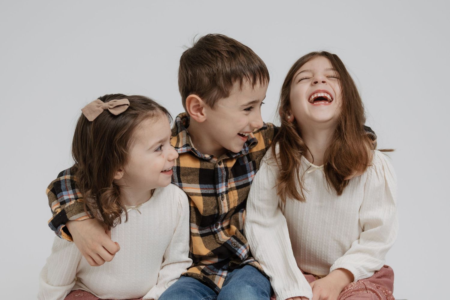 A family shares joyful laughter together while sitting on a light colored couch in a candid photo series.