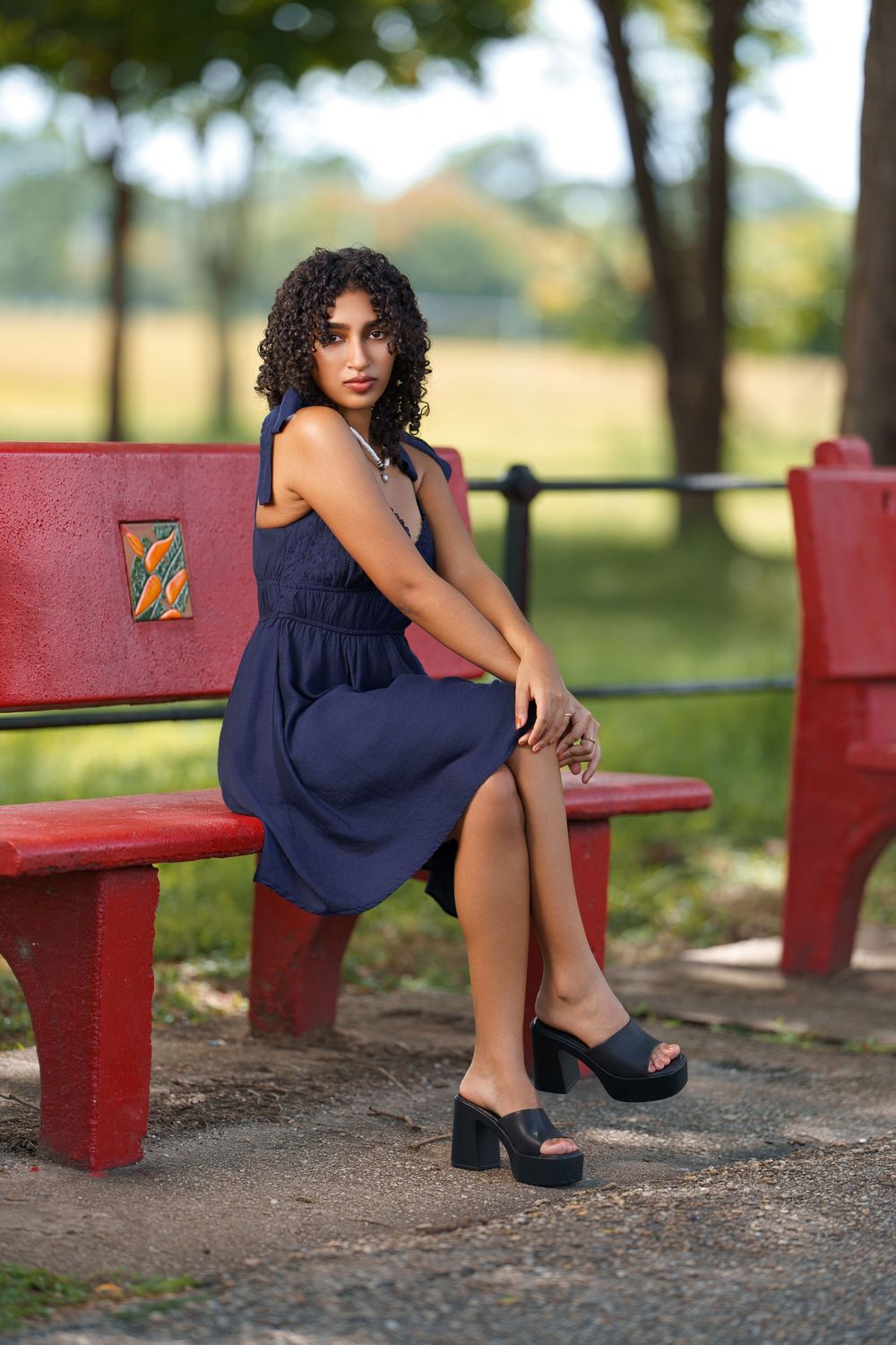 A person in a navy blue dress sits on red painted benches in an outdoor park setting.