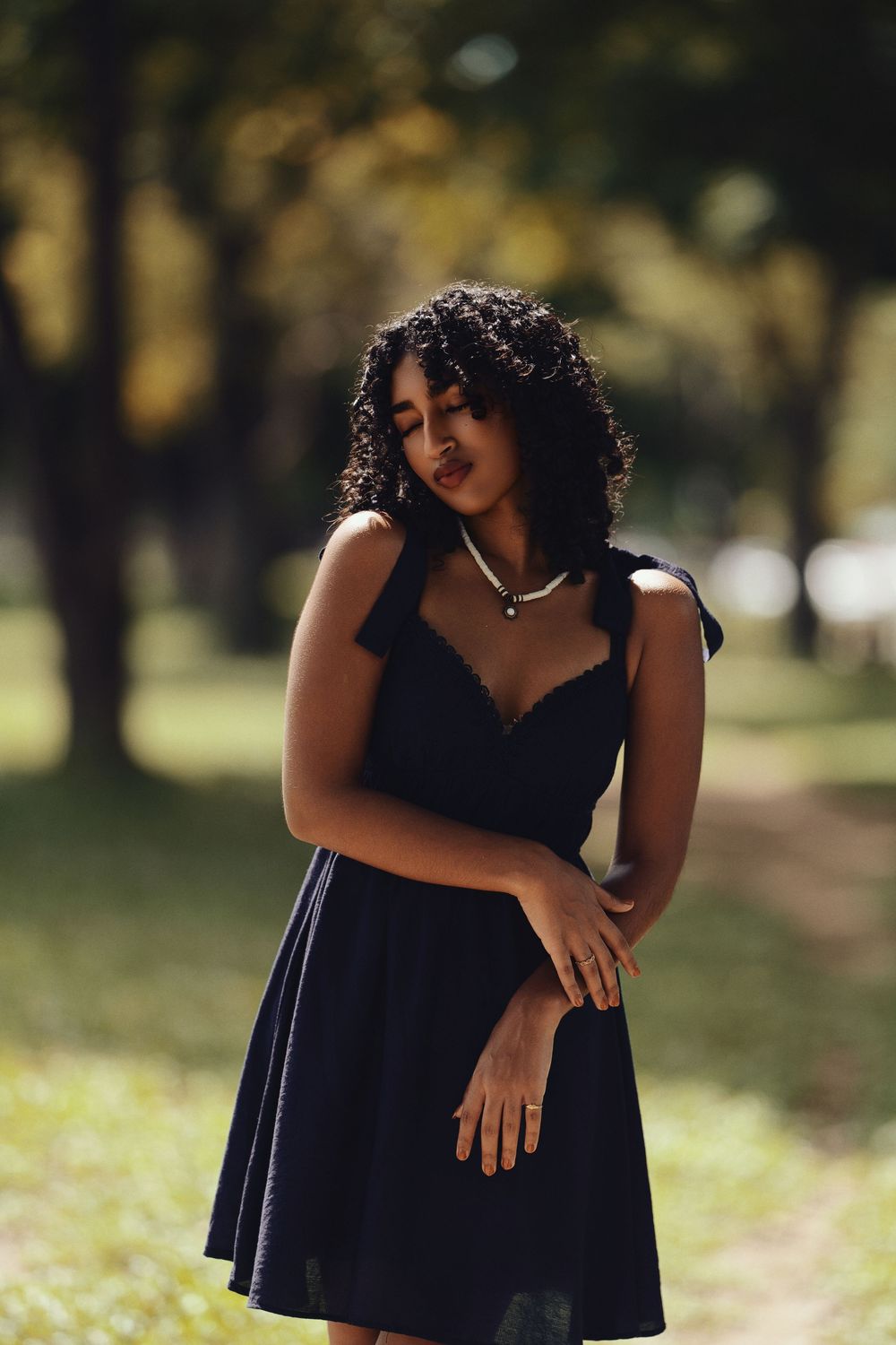 A navy blue dress is worn outdoors in a park setting with soft natural lighting and bokeh background effects.