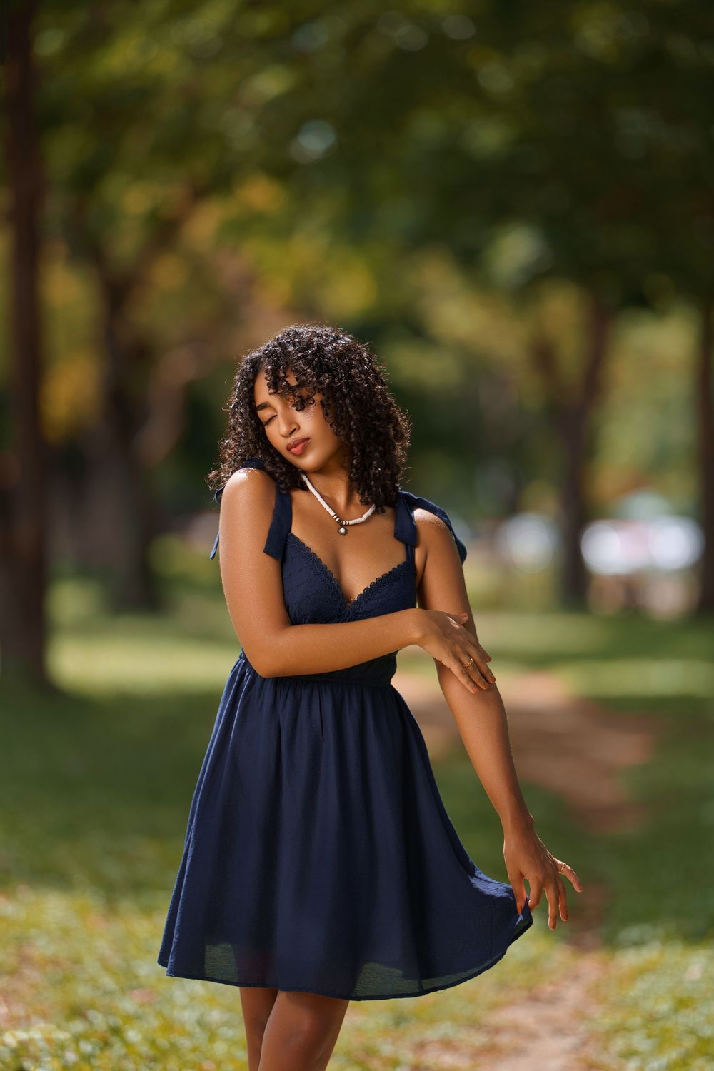 A woman in a navy blue dress twirls gracefully in a sunlit park setting during an outdoor photo session.