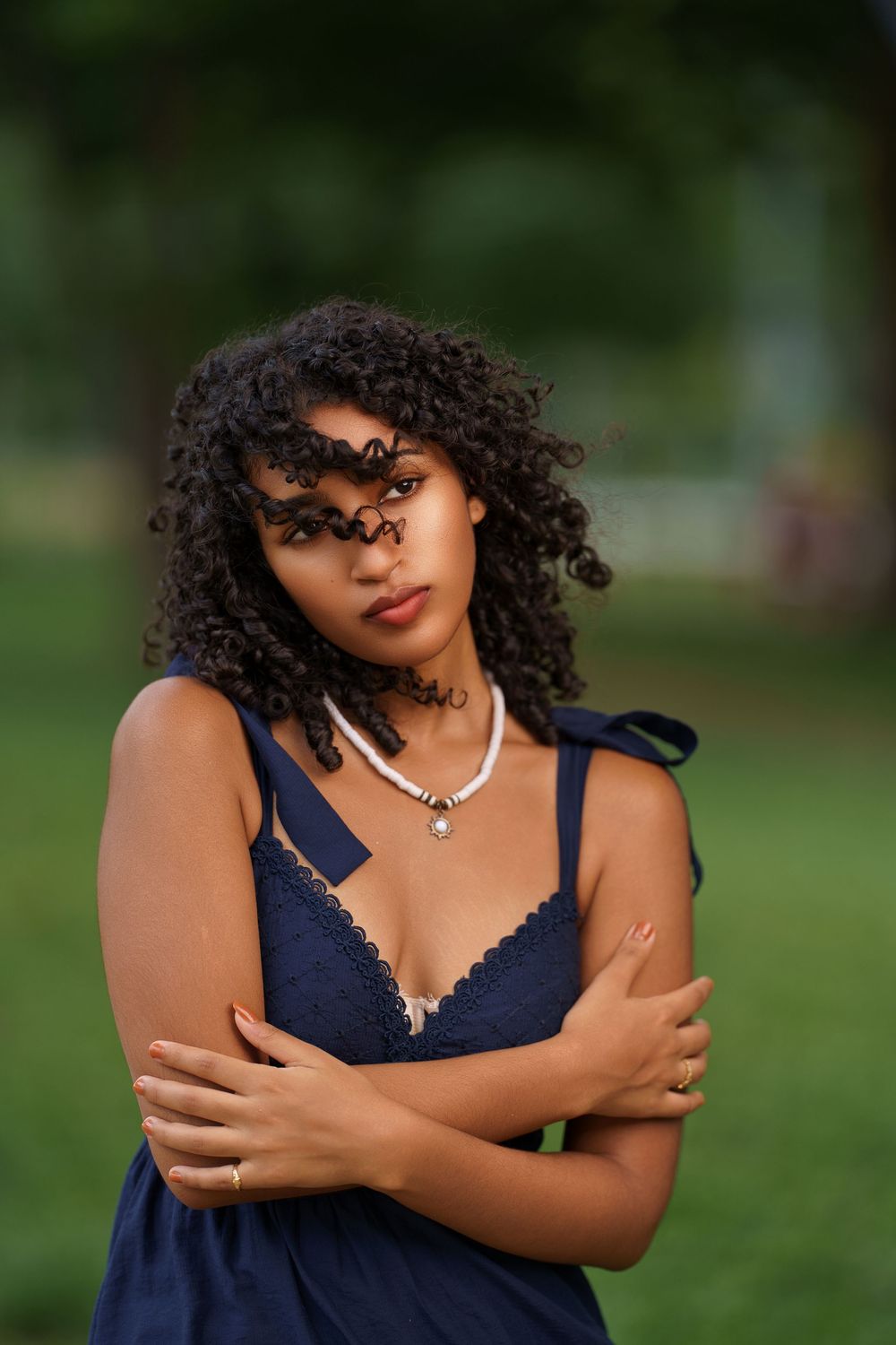 A person in a navy blue dress poses confidently outdoors with natural curly hair and silver necklace.