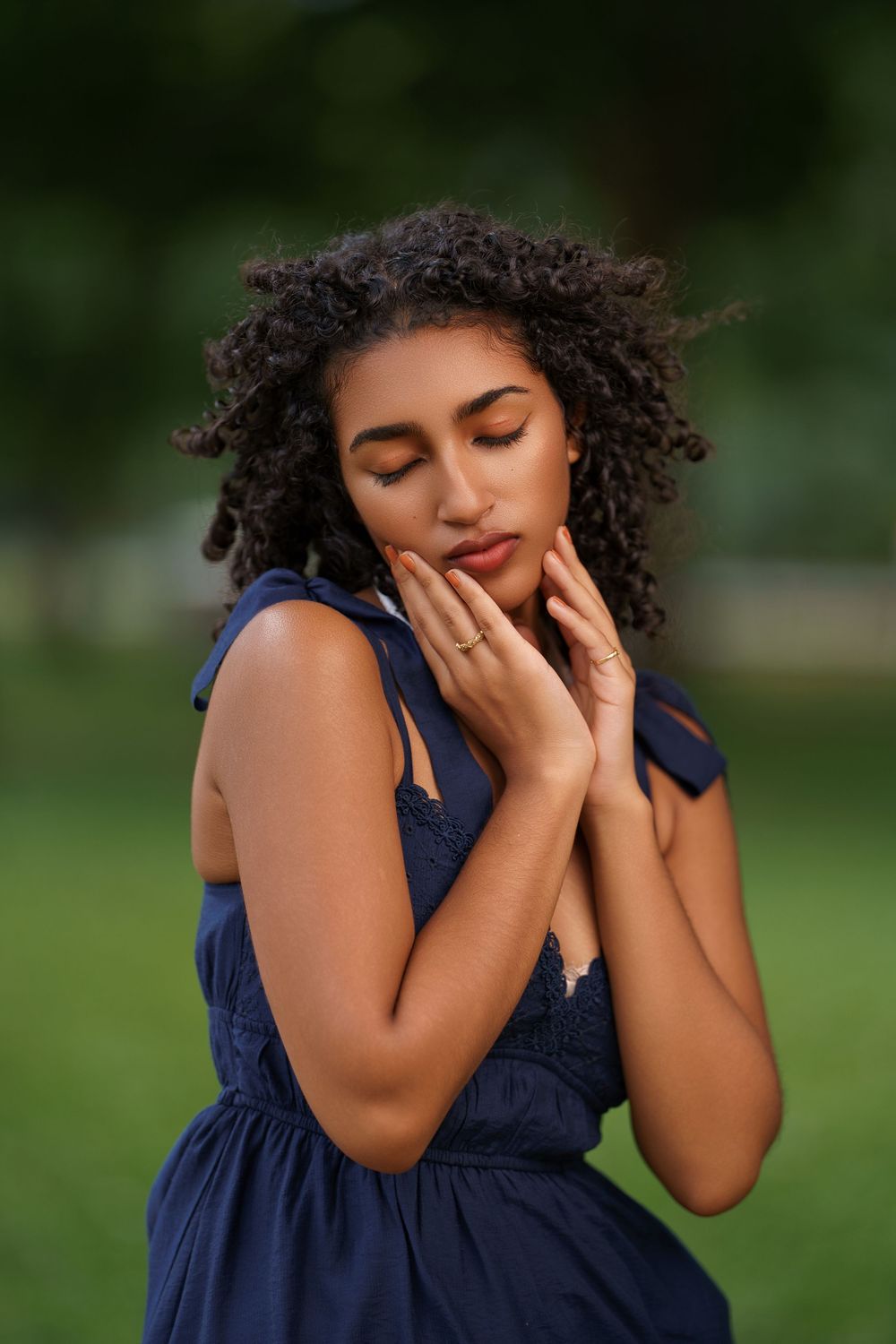 A candid moment captured of someone in a navy dress with curly hair expressing joy in a garden setting.