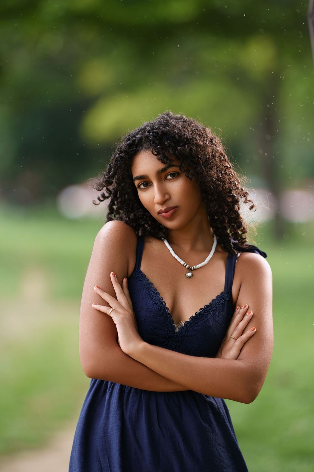 A person in a navy blue dress poses outdoors in a park setting with natural greenery in the background.