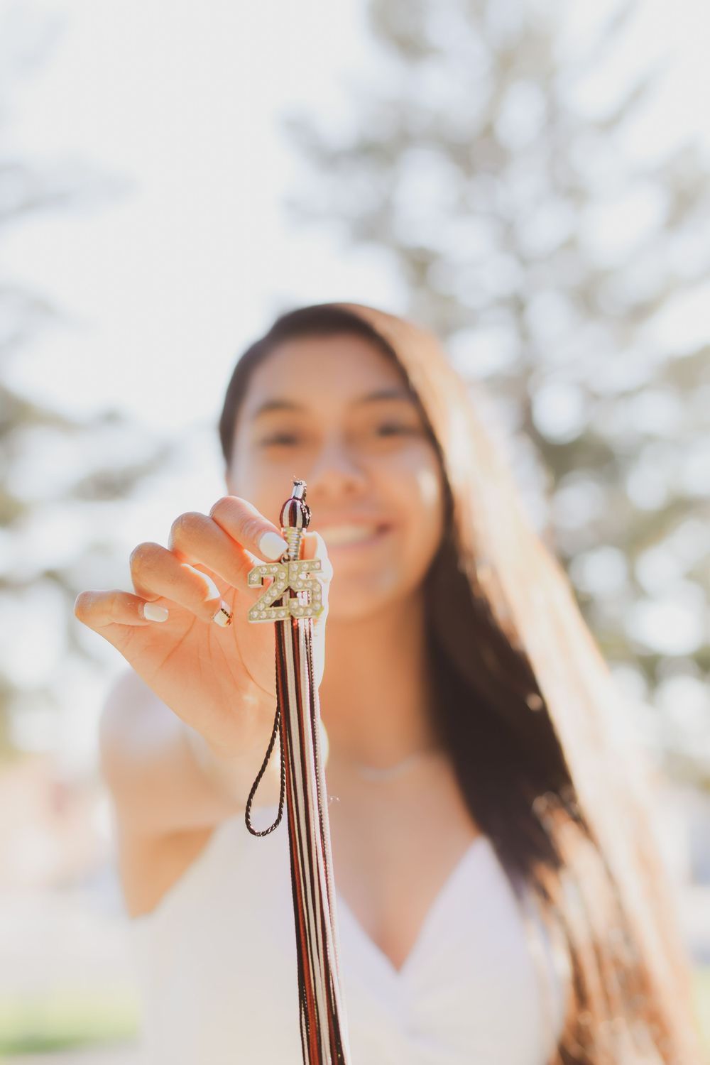 Woman holding up delicate gold jewelry against blurred outdoor background with soft natural lighting.