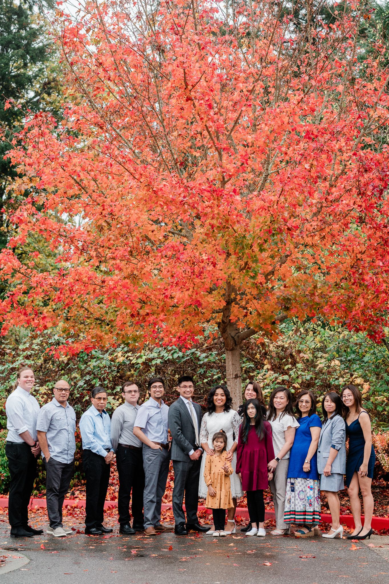 A group of family gathered beneath a vibrant coral-colored maple tree in autumn.