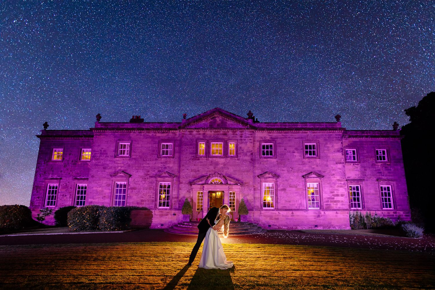 Historic building illuminated in purple and gold lighting against starry night sky for evening wedding reception.