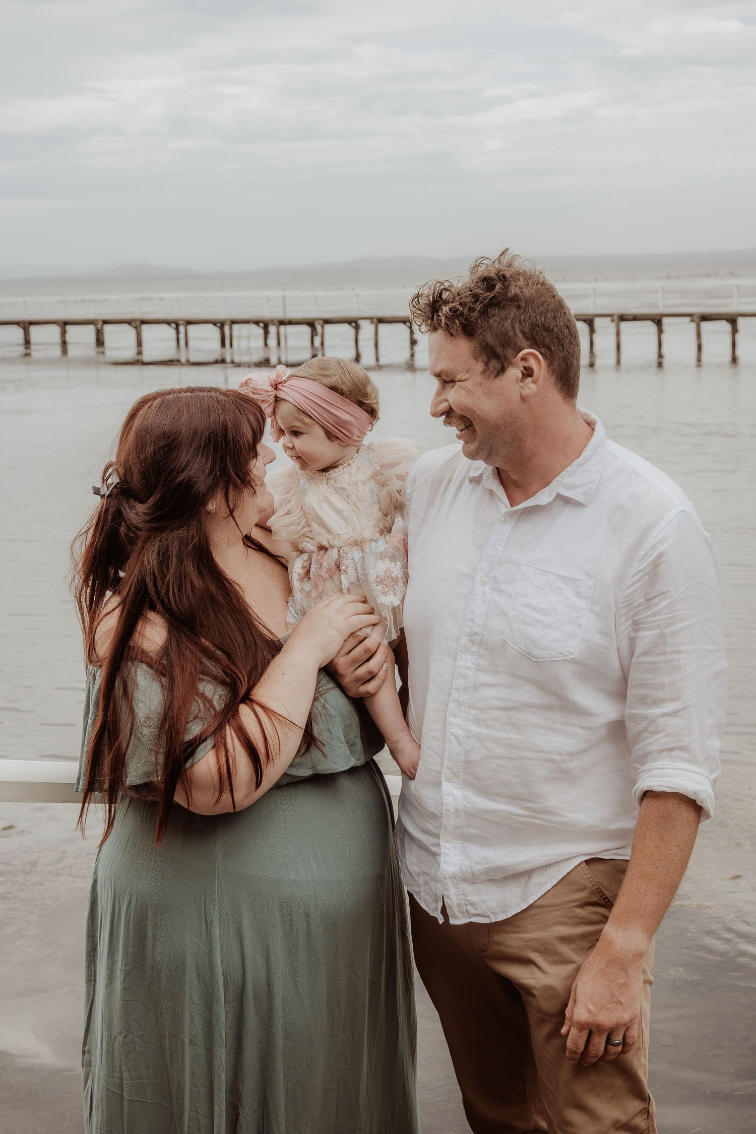 Intimate family moment shared by the water with a pier in the distance at a central coast christmas photoshoot.