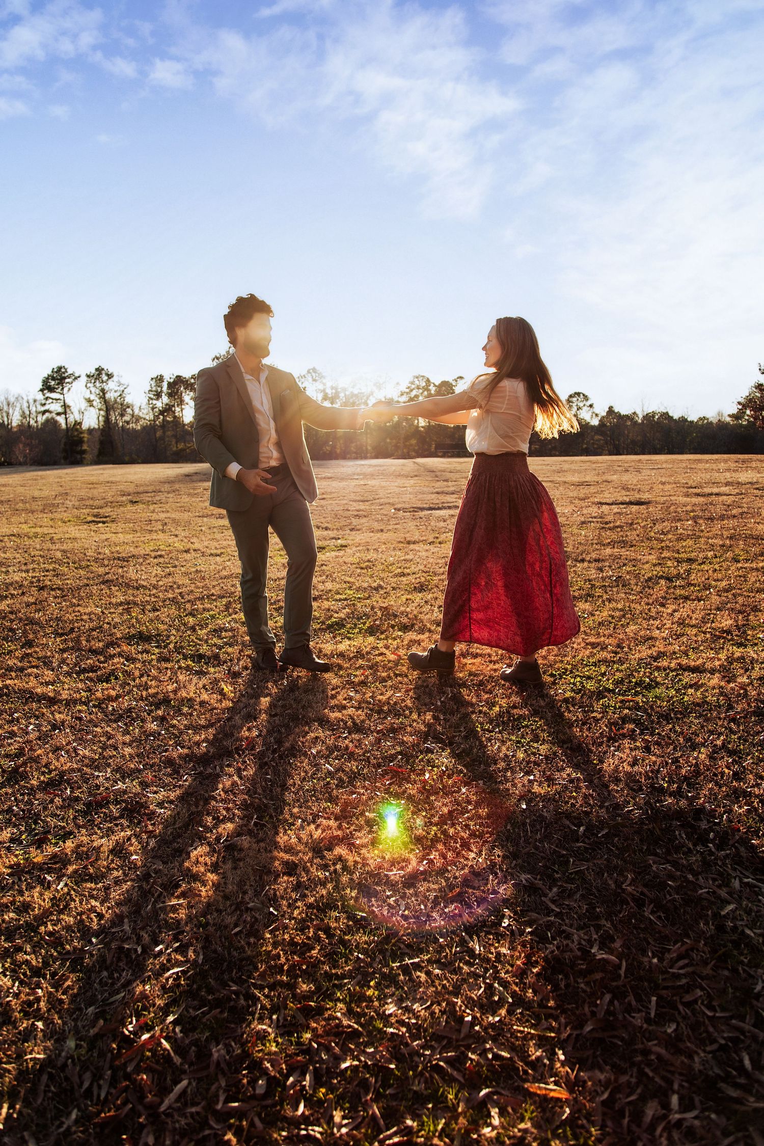 Couple walking through a golden field at sunset casting long shadows.