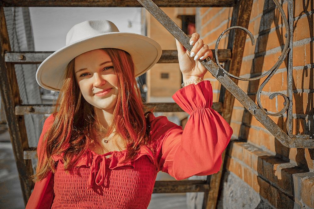 A person in a red sweater poses cheerfully in front of a rustic wooden wall with decorative elements.