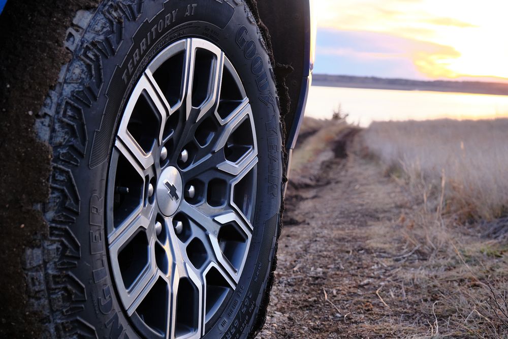 Close-up view of rugged off-road tires and alloy wheels on a vehicle against a desert landscape at sunset.